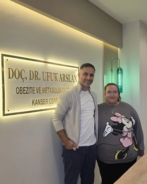 Doç. Dr. Ufuk Arslan muayenehanesinde, muayene odasındaki tabelanın önünde